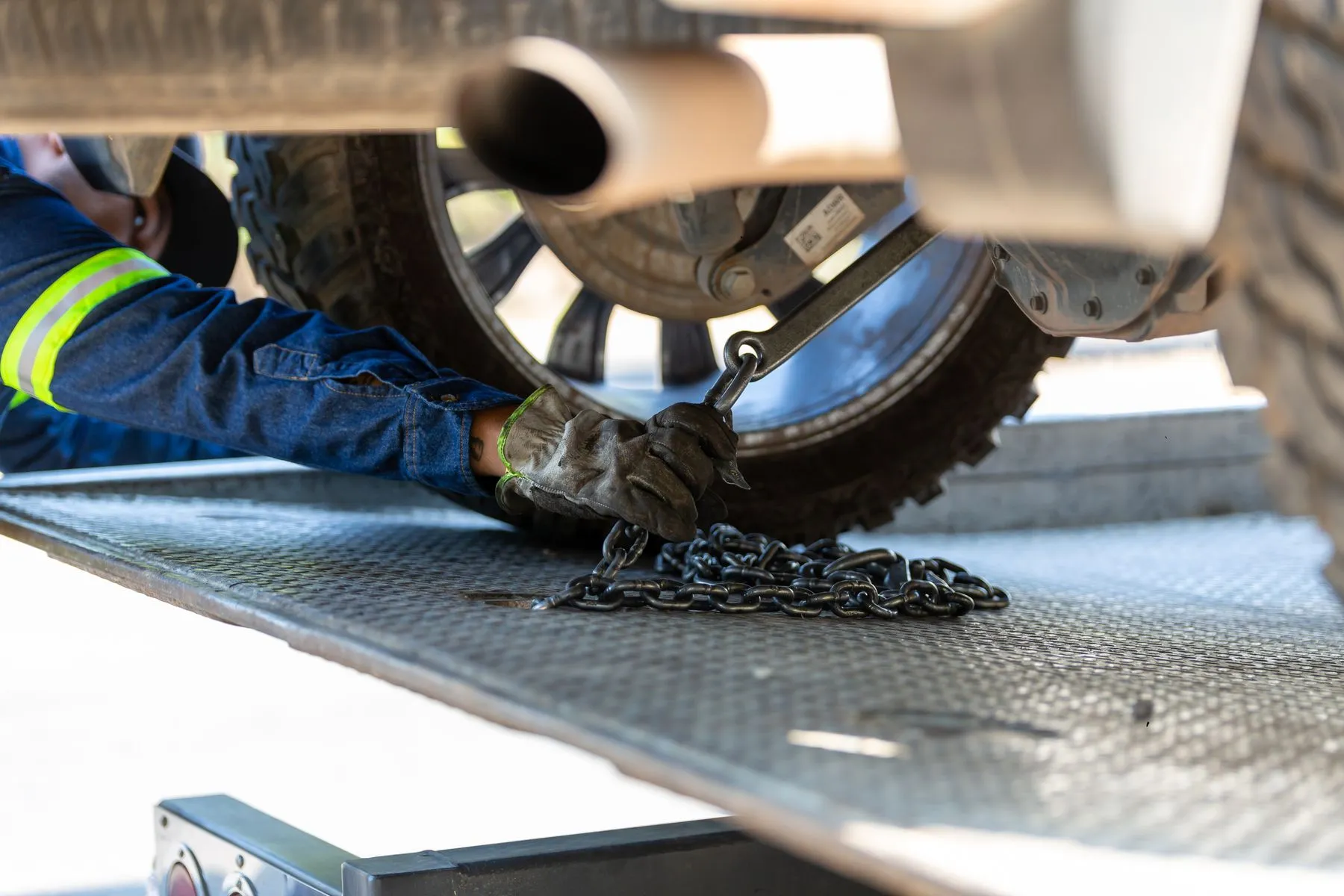 A tow operator's gloved hand securing a car's wheel to a flatbed with a chain