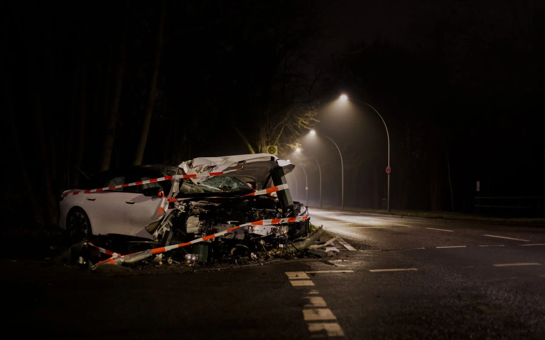 A wrecked car with a crushed front end wrapped in red and white tape on a dark street