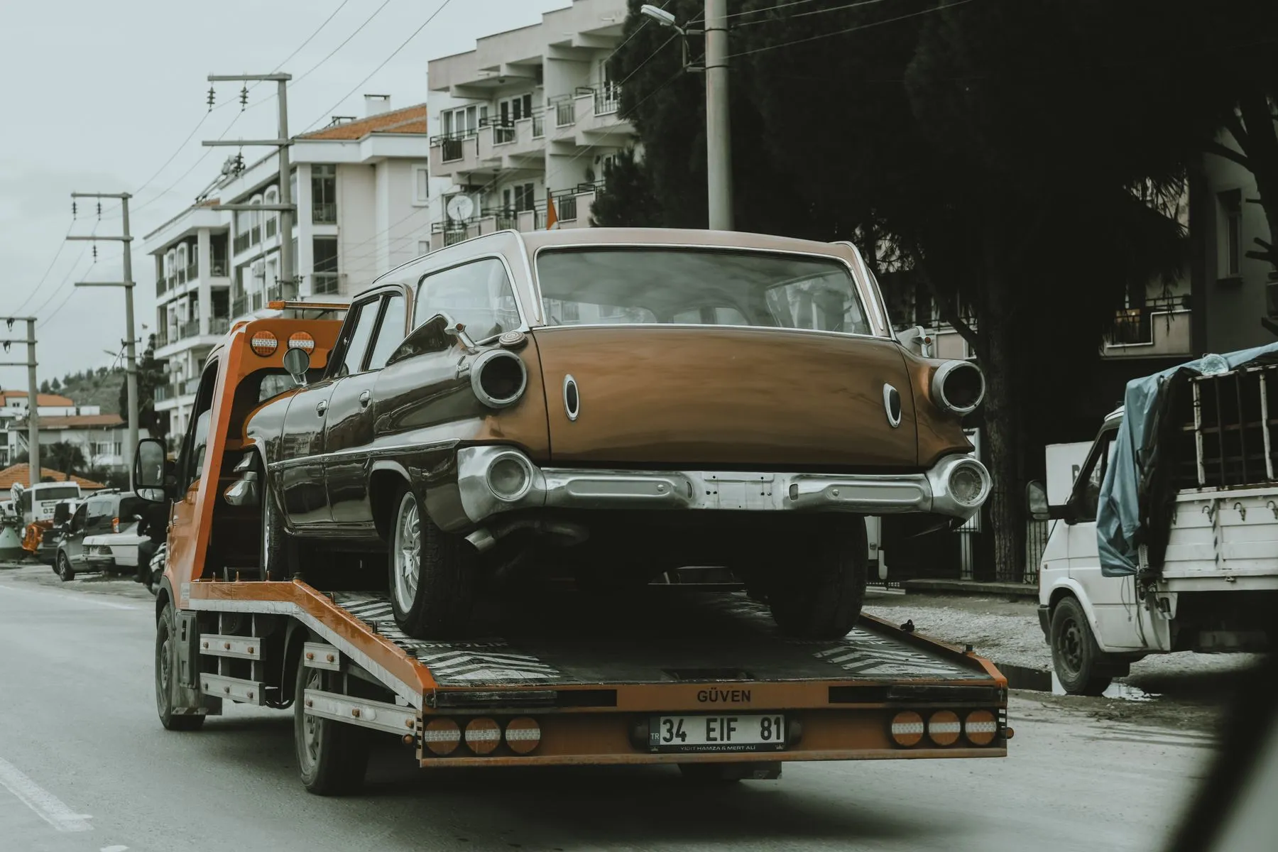 A tow truck carrying an old car through a city street